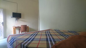 A room with a bed, a television mounted on the wall, a small wooden table, and a chair. - Purnama Raya Guest House (Pematangsiantar)