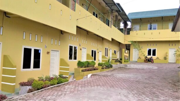 A yellow building with multiple windows and doors, a paved courtyard, and a motorcycle parked outside.