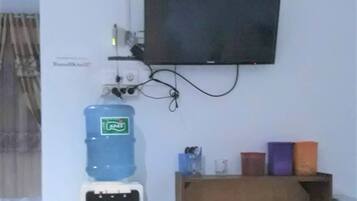 Habitación con televisión montada, dispensador de agua y una estantería con objetos varios.
