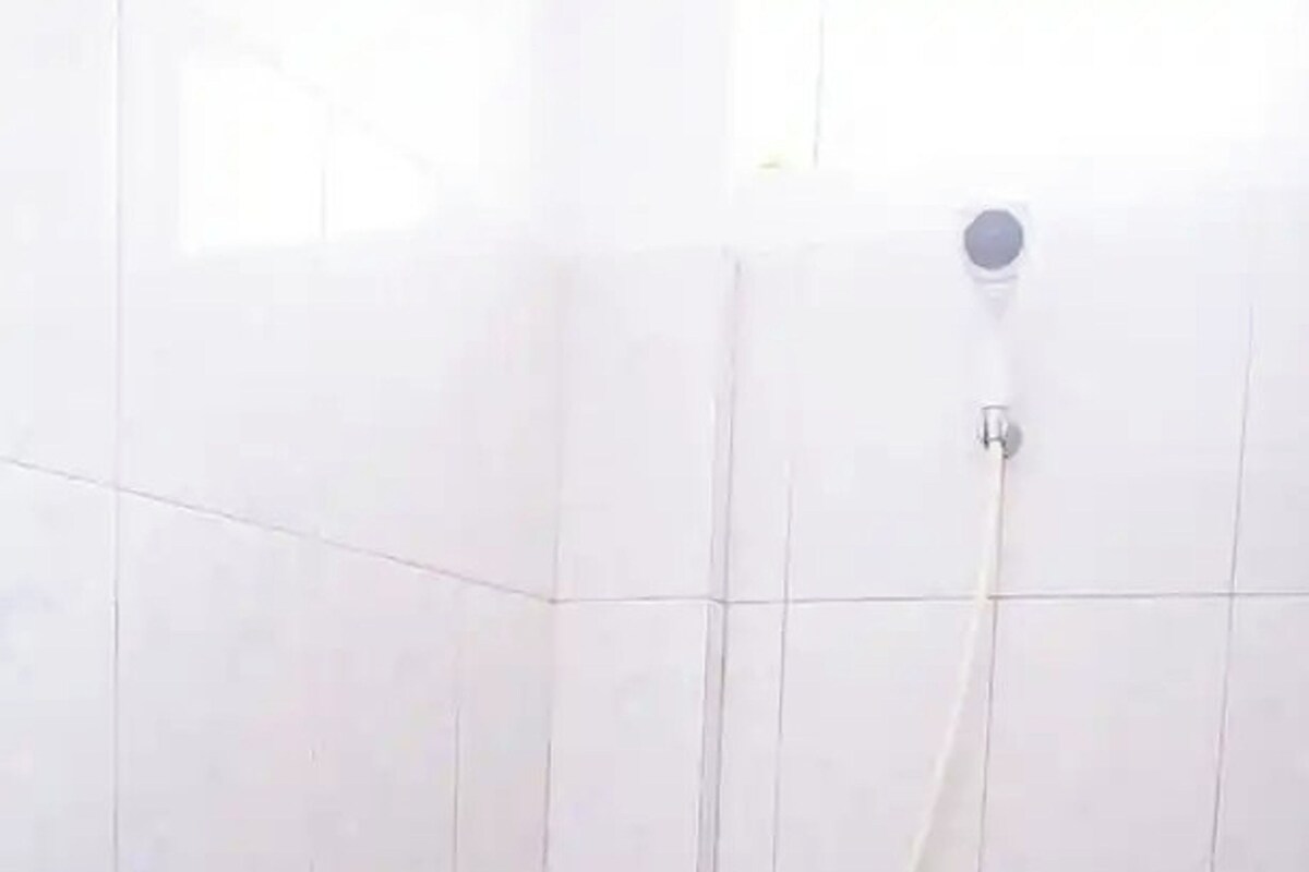 A bathroom with white tiles and a shower head.