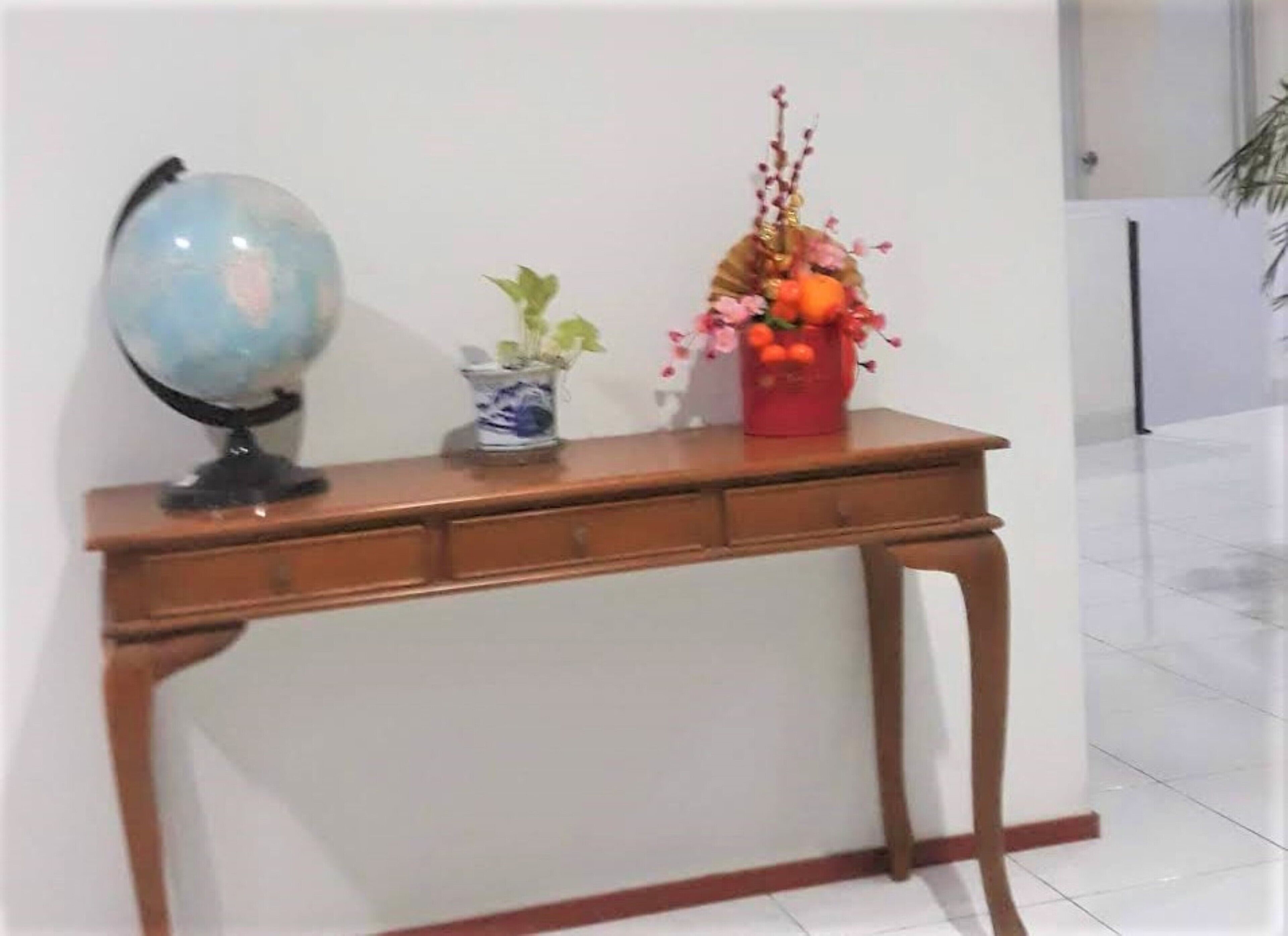 A wooden console table with a globe, a blue and white vase with green plants, and a red vase with orange flowers.