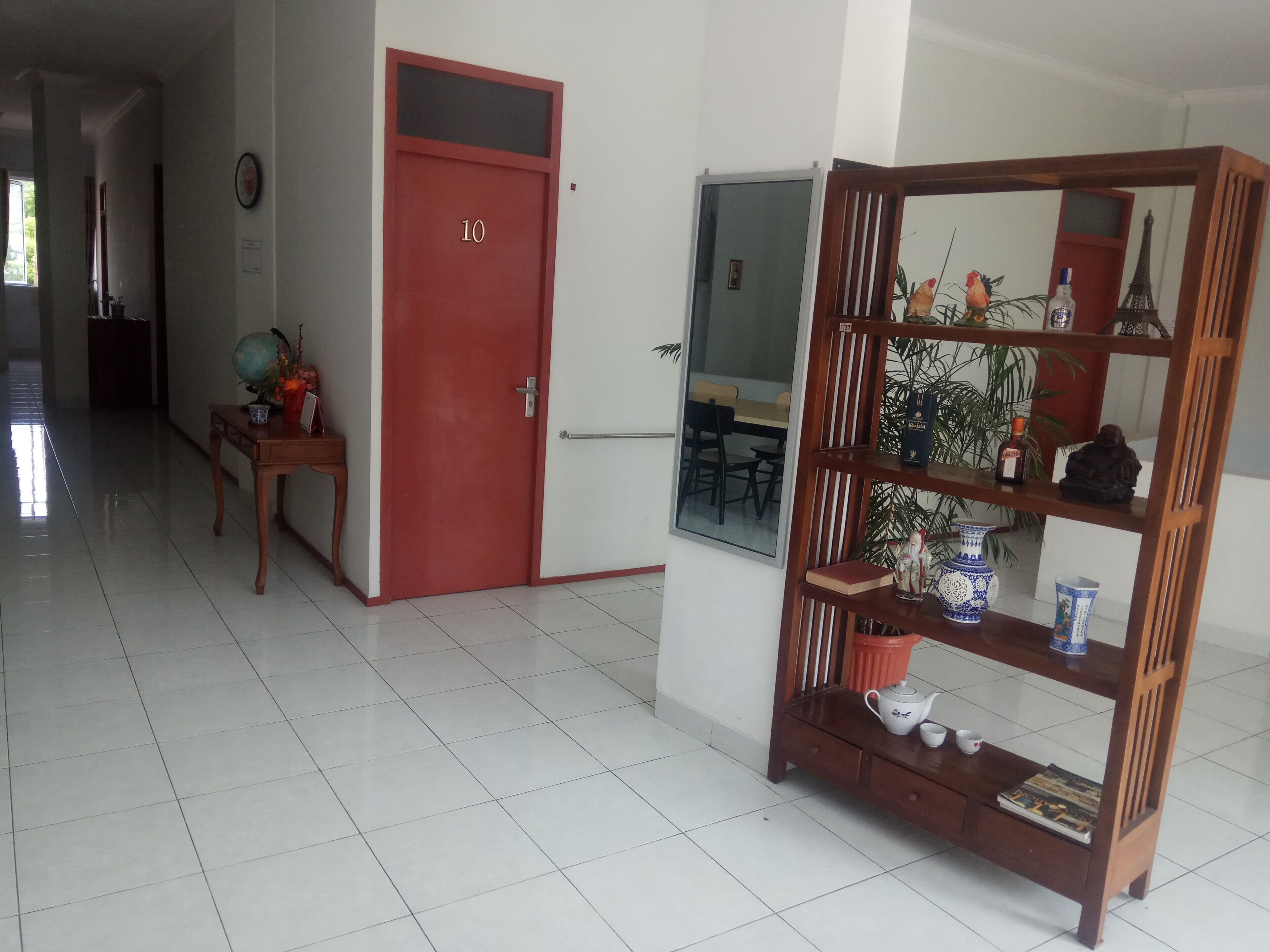 A hallway with a red door labeled '10', a wooden side table with a globe and flowers, and a wooden bookshelf with decorative items.