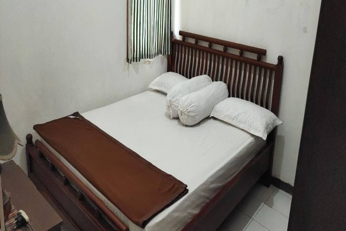 A single-bed room with a wooden headboard, white bedding, and a brown throw blanket.