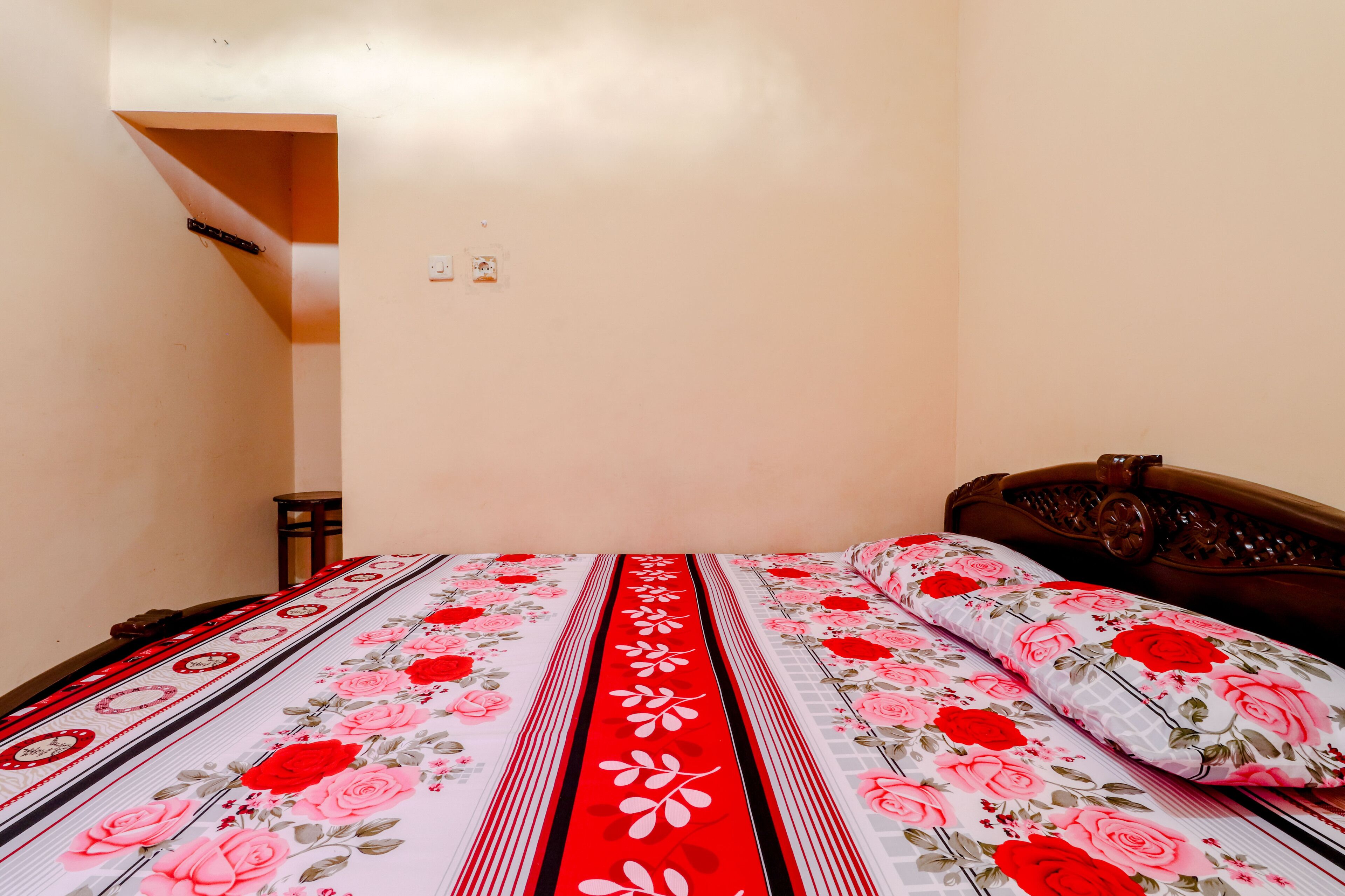 A bedroom with a bed, a wooden headboard, and a wall-mounted light switch.