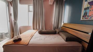 A hotel room with a bed, curtains, a window, and a wall with a colorful painting.