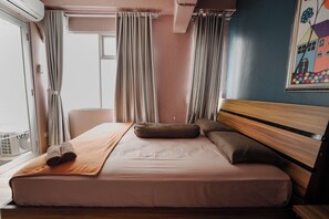 A hotel room with a bed, curtains, a window, and a wall with a colorful painting. - The Jarrdin by Bethania Pro by Zuzu (Bandung)
