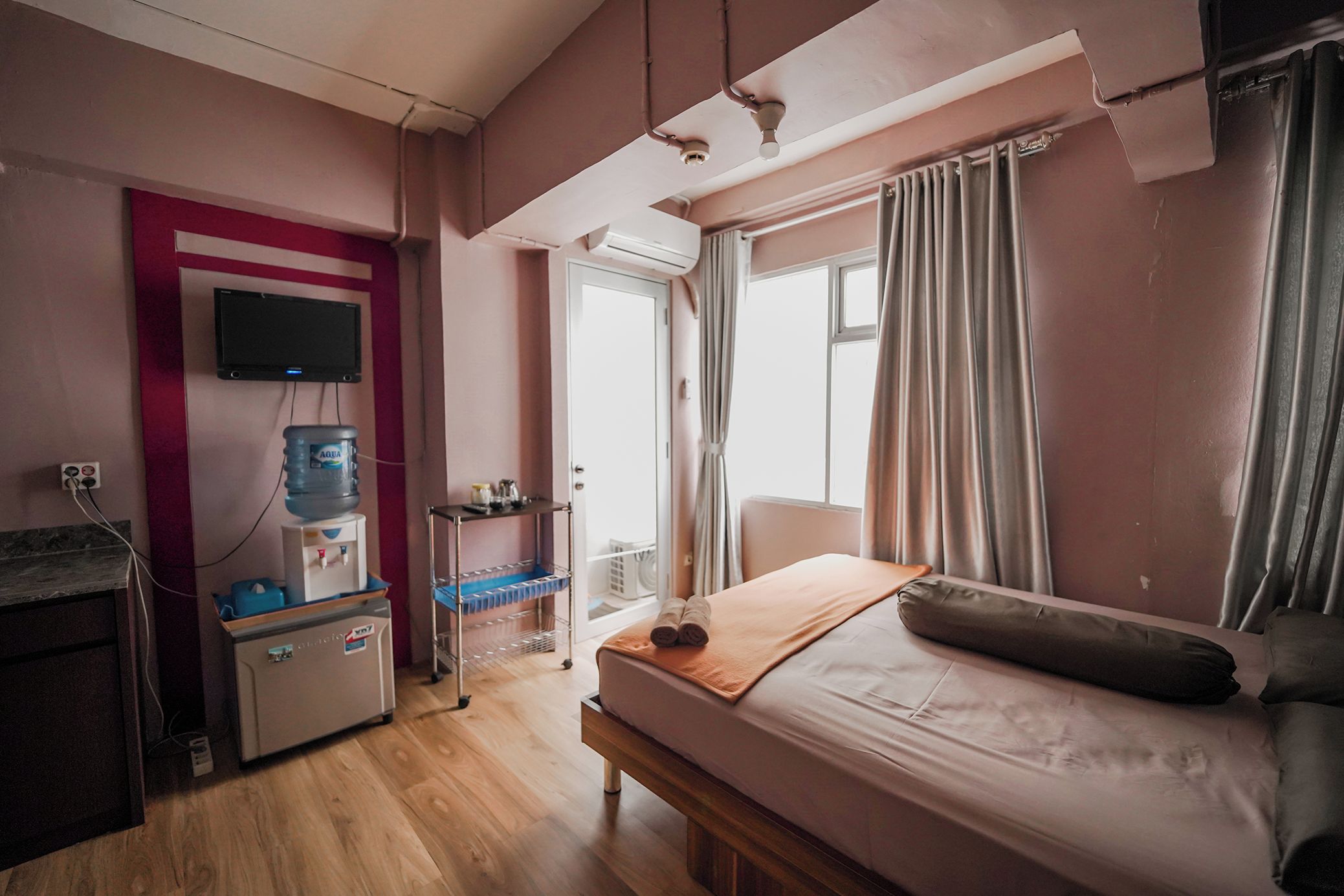 A hotel room with a bed, a desk with a water dispenser, a television, and a window with curtains.