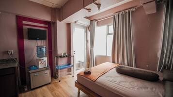 A hotel room with a bed, a desk with a water dispenser, a television, and a window with curtains.