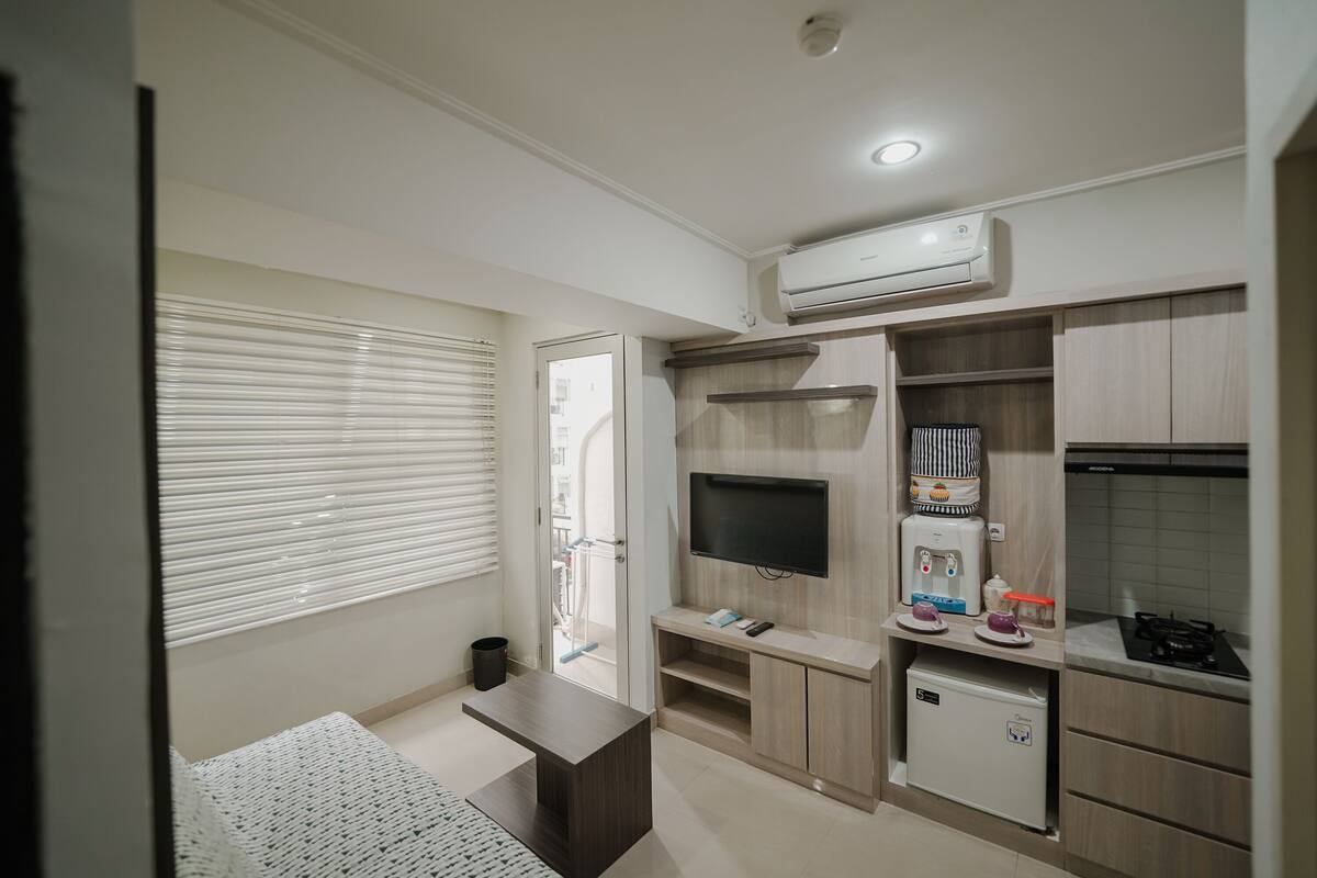 Un espacio habitable pequeño con kitchenette, televisor y refrigerador compacto.
