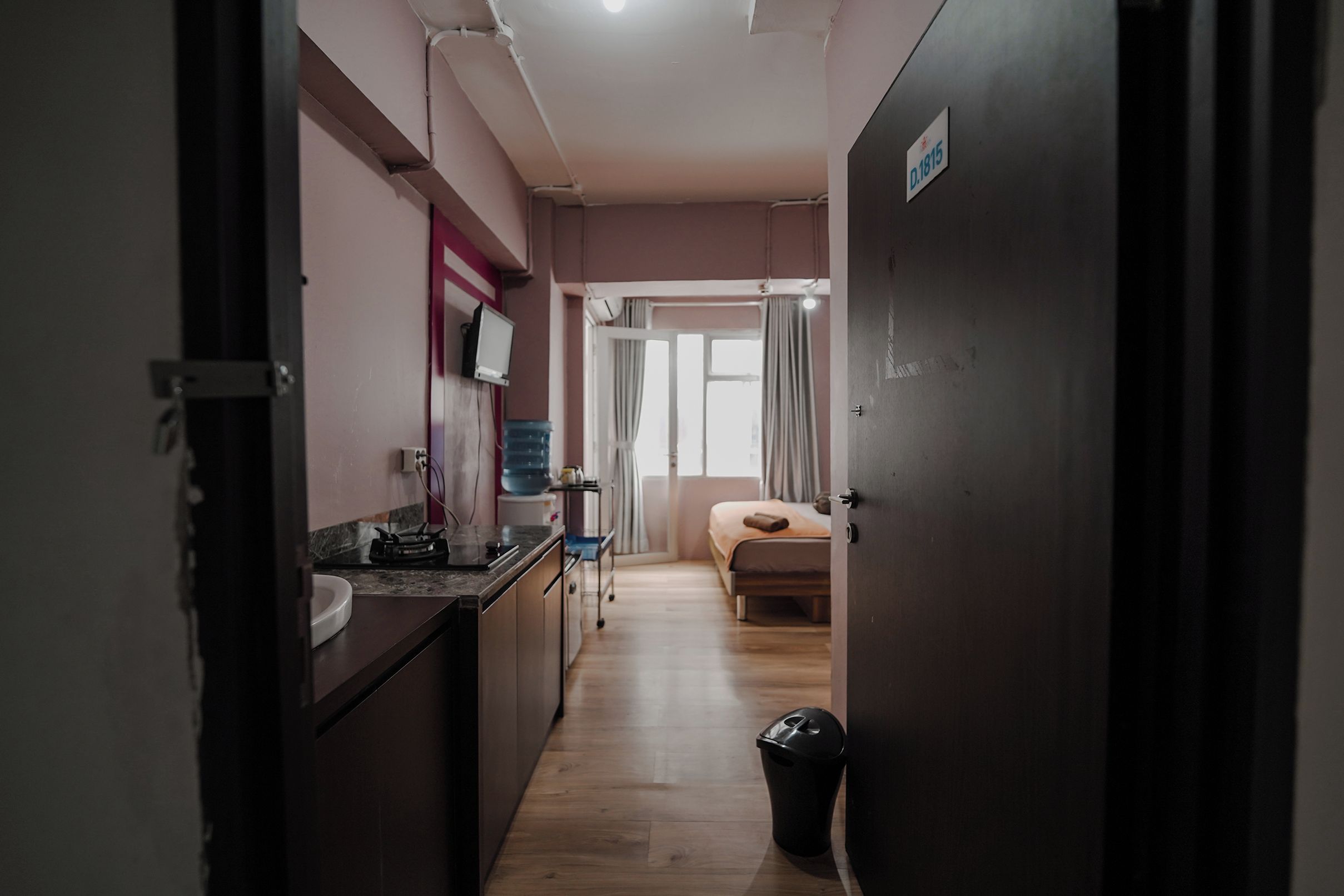 A narrow hallway leading to a bedroom with a bed and a window.