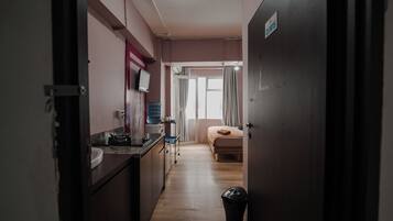 A narrow hallway leading to a bedroom with a bed and a window.