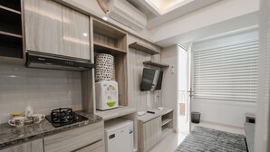A modern kitchen with a built-in stove, a small refrigerator, and a microwave. There is a TV mounted on the wall and a window with blinds. - The Jarrdin by Bethania Pro (Bandung)