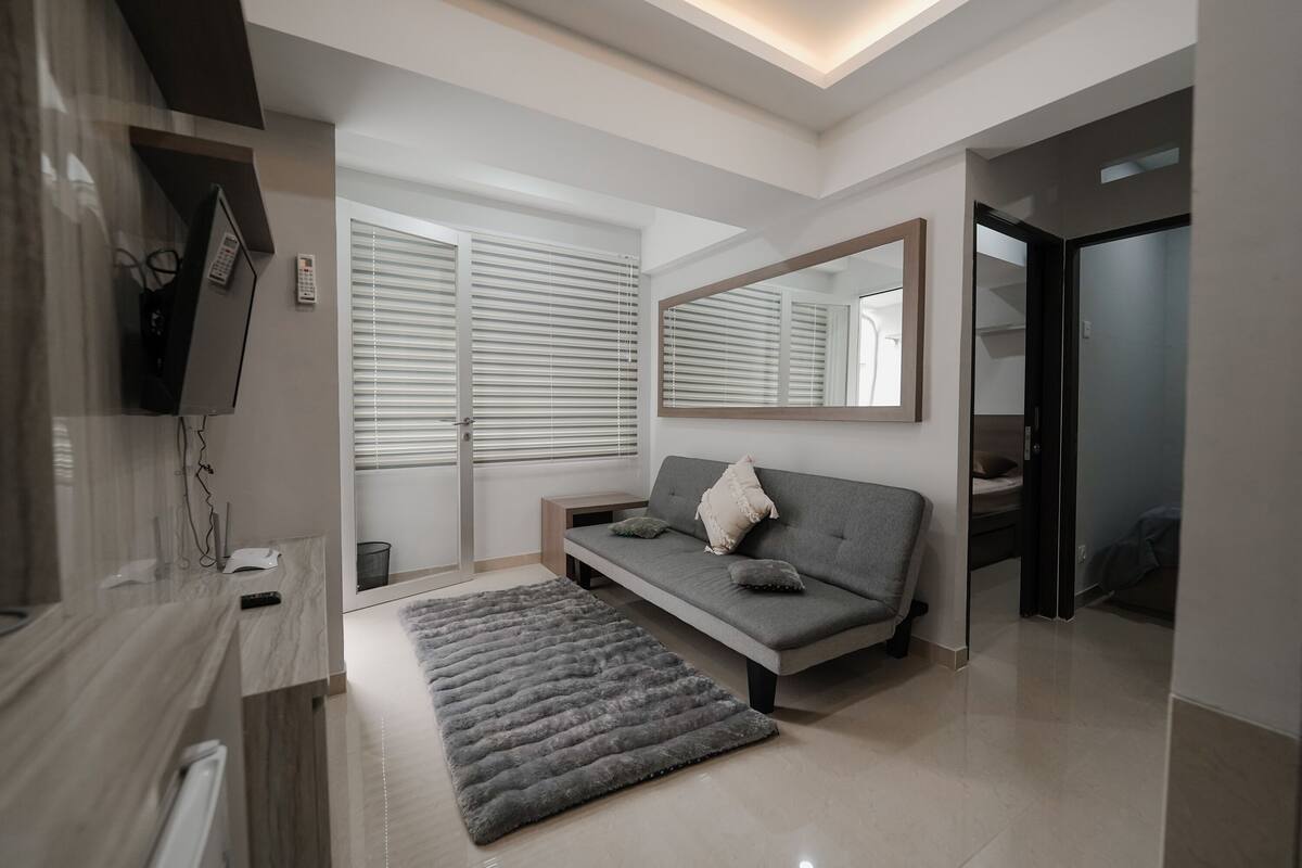 Una sala moderna con un sofá gris, un espejo grande y un tapete gris.