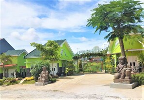 A row of green buildings with a central archway, surrounded by statues and greenery.