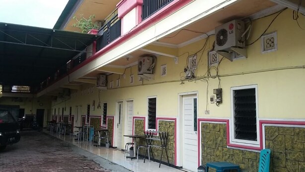 A building with multiple rooms, some with doors and windows, and a covered outdoor area with tables and chairs. - Griya Dua Putra Jaya I (Bojonegoro)