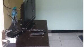 A room with a desk, a television, and a computer. There is a water bottle on the desk. - Griya Dua Putra Jaya I (Bojonegoro)
