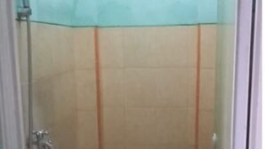 A small, enclosed bathroom with a toilet, a green bucket, and a showerhead. - Griya Dua Putra Jaya I (Bojonegoro)
