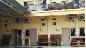 Un immeuble à plusieurs étages doté de balcons, de climatiseurs et d’un espace extérieur aménagé avec des sièges.