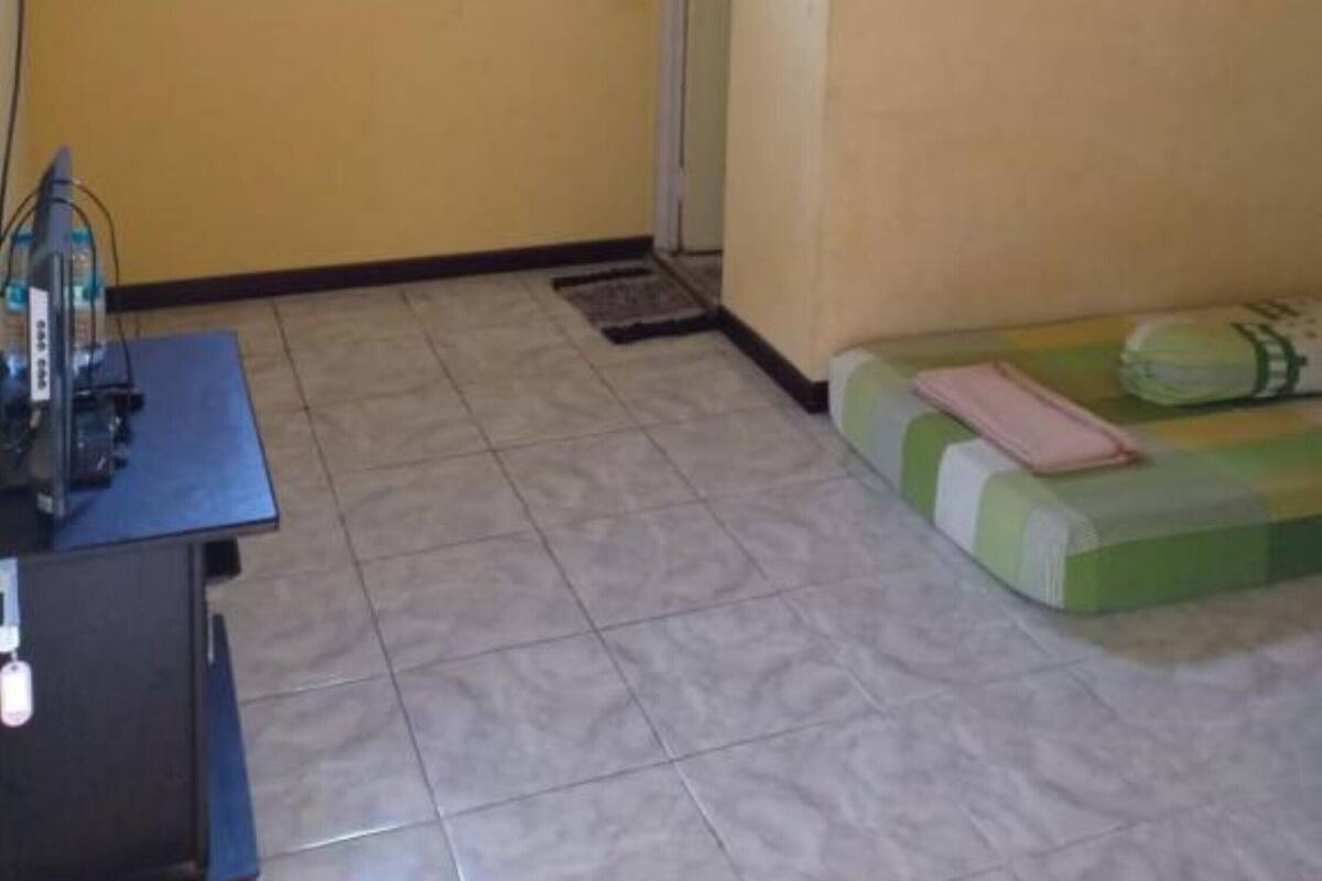 A room with a tiled floor, a desk with electronic equipment, a bed with a green and white mattress, and a door with a small window.