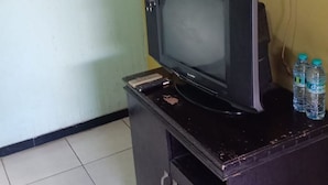 Un téléviseur posé sur un meuble en bois, avec une prise électrique et deux bouteilles d’eau sur le côté droit.