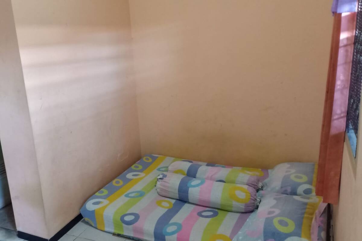 A small, narrow room with a bed covered in colorful bedding.