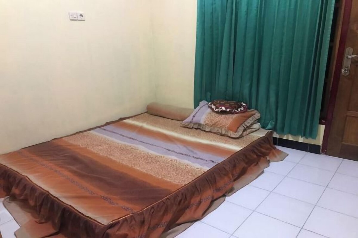 A small, neatly made bed with a striped bedspread and a decorative pillow, a green curtain, and a tiled floor.