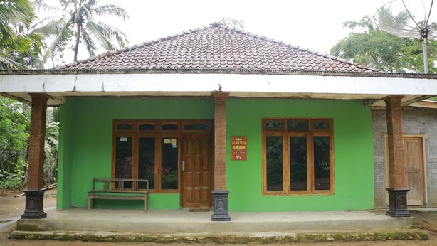 A green building with a tiled roof, a wooden door, and a bench outside. - Homestay Jemiran (Kokap)