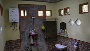 A bathroom with a shower, a toilet, a sink, and a mirror. There are windows and a wall-mounted heater. - Homestay Jemiran (Kokap)