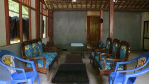 A room with wooden furniture and blue plastic chairs, a small table, and a door leading outside. - Homestay Jemiran (Kokap)