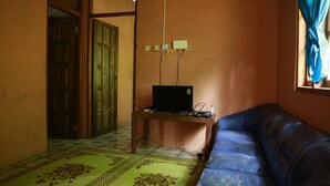 A room with a blue sofa, a small table with a laptop, a patterned rug, and a door. - Homestay Jemiran (Kokap)