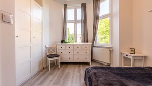 A bedroom with a bed, a dresser, a chair, a window with curtains, and a radiator. - Victus Apartamenty - Penthouse 1 (Sopot)