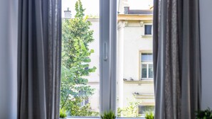 A window with curtains, a view of a building, and two potted plants on the windowsill. - Victus Apartamenty - Penthouse 1 (Sopot)