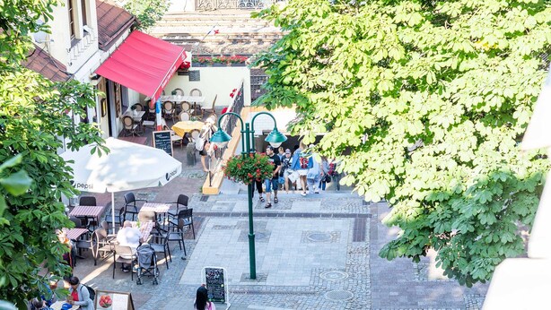 An outdoor café area with tables and chairs, surrounded by greenery and buildings. - Victus Apartamenty - Penthouse 1 (Sopot)