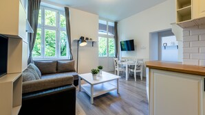 A modern living room with a sofa, a coffee table, and a TV. There is a dining area with a table and chairs, and a kitchen area with a counter and cabinets. - Victus Apartamenty - Penthouse 1 (Sopot)