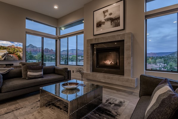 A modern living room with a fireplace, large windows, and a view of the mountains.