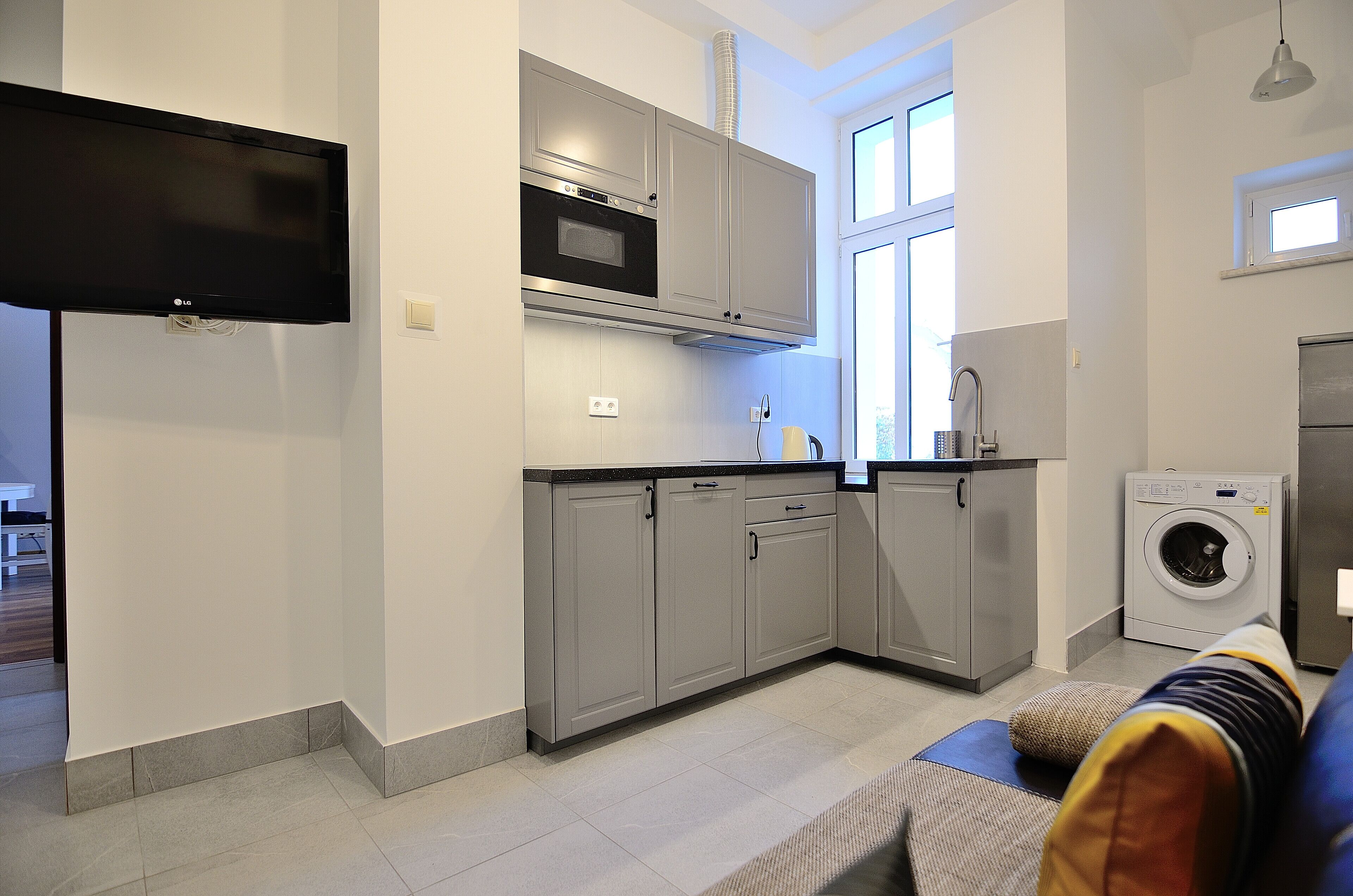A modern kitchen with grey cabinets, a built-in oven, and a washing machine.