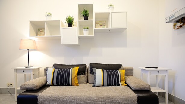 A modern bedroom with a bed, bedside tables, a lamp, and built-in shelving with plants. - Victus Apartamenty - Penthouse 2 (Sopot)