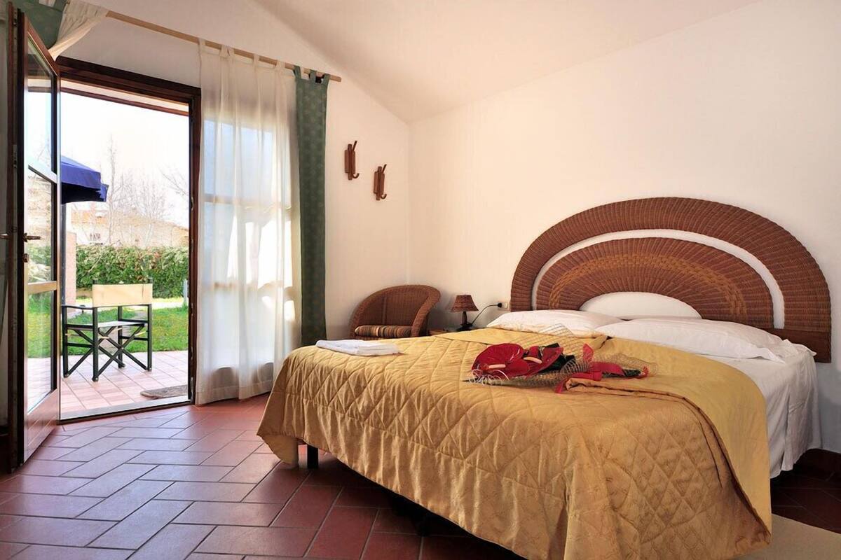 Ein Hotelzimmer mit Bett, Stuhl, Tisch und Blick ins Freie.