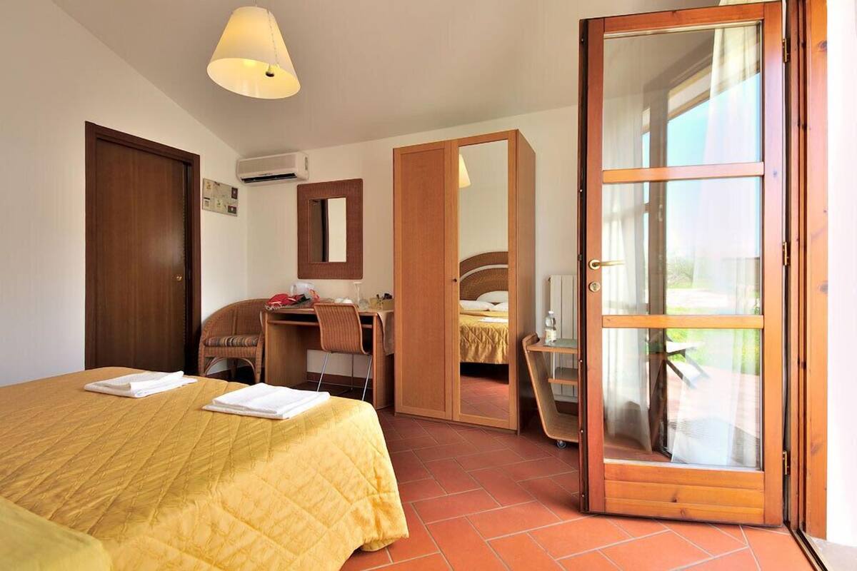 Ein Hotelzimmer mit einem Bett, einem Schreibtisch, einem Stuhl, einem Kleiderschrank und einer Glasschiebetür.
