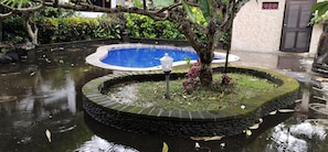 A circular stone pool with a blue center, surrounded by a stone border, and a tree in the middle. - Puri Rasa Ubud (Sukawati)