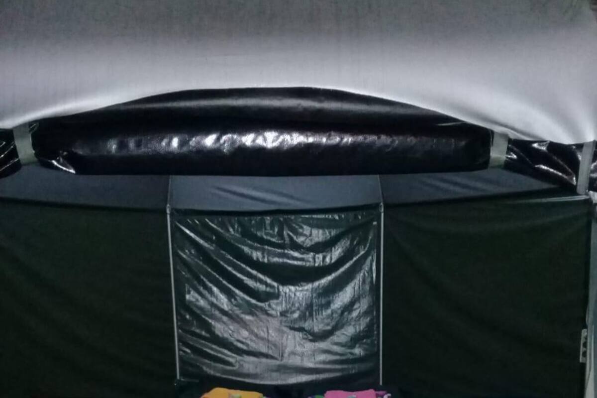 A tent with a black interior, a metal frame, and a central black curtain. There are colorful pillows and a metal table in front.
