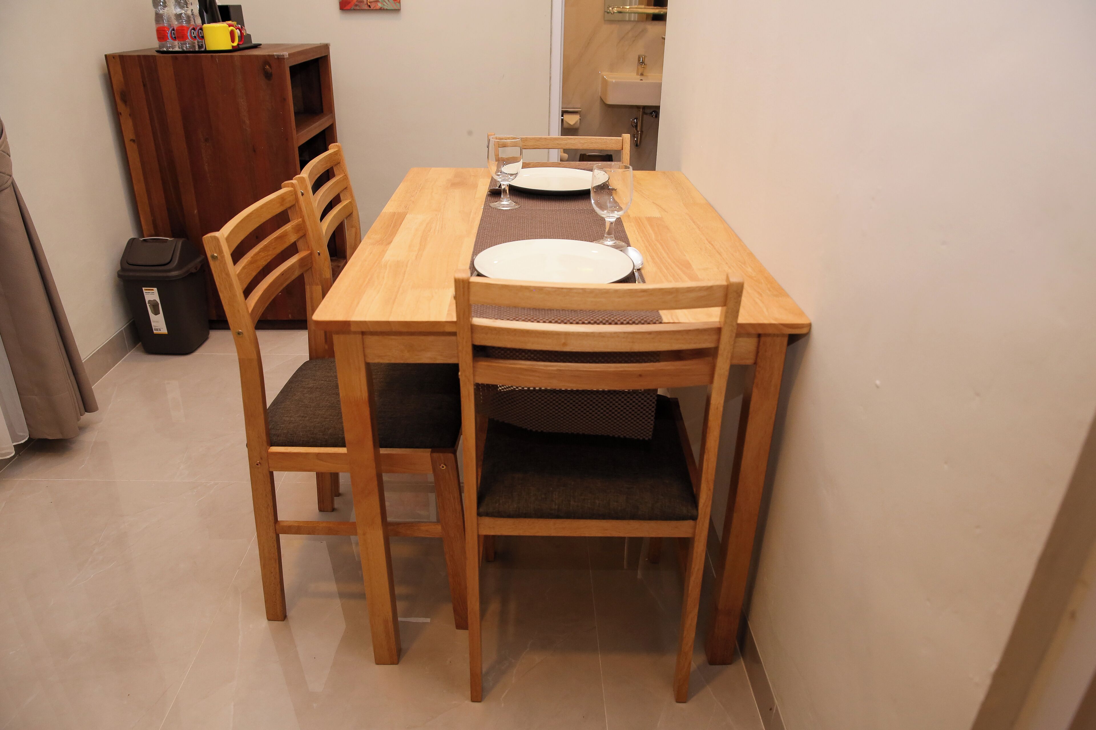 Une table de salle à manger en bois, avec quatre chaises, un set de table et deux verres à vin.
