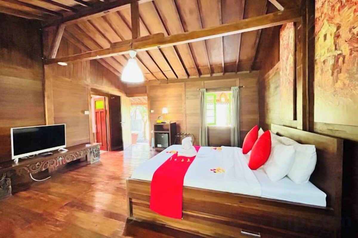 A wooden room with a bed, a TV, and a door leading to another room.