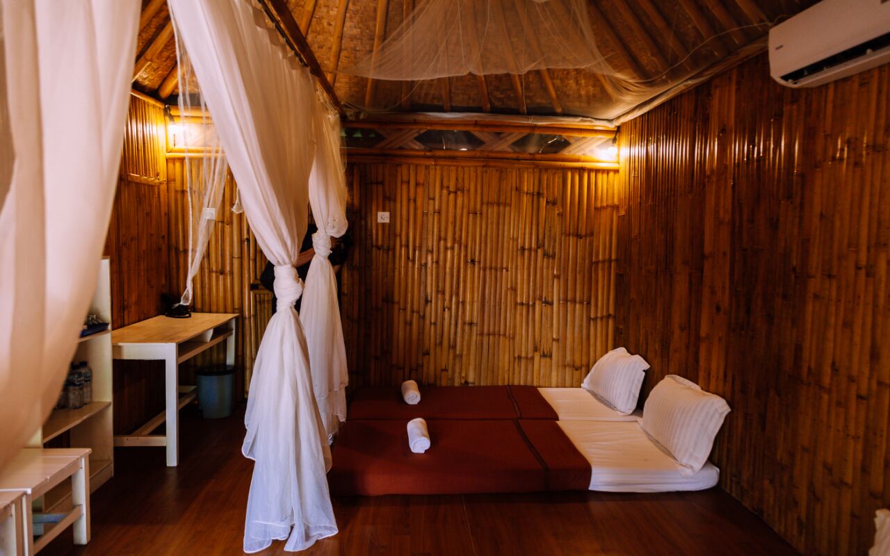 Ein Zimmer mit einer Holzwand, einem Bett mit weißer Bettwäsche, einem kleinen Tisch und einem hängenden Baldachin.