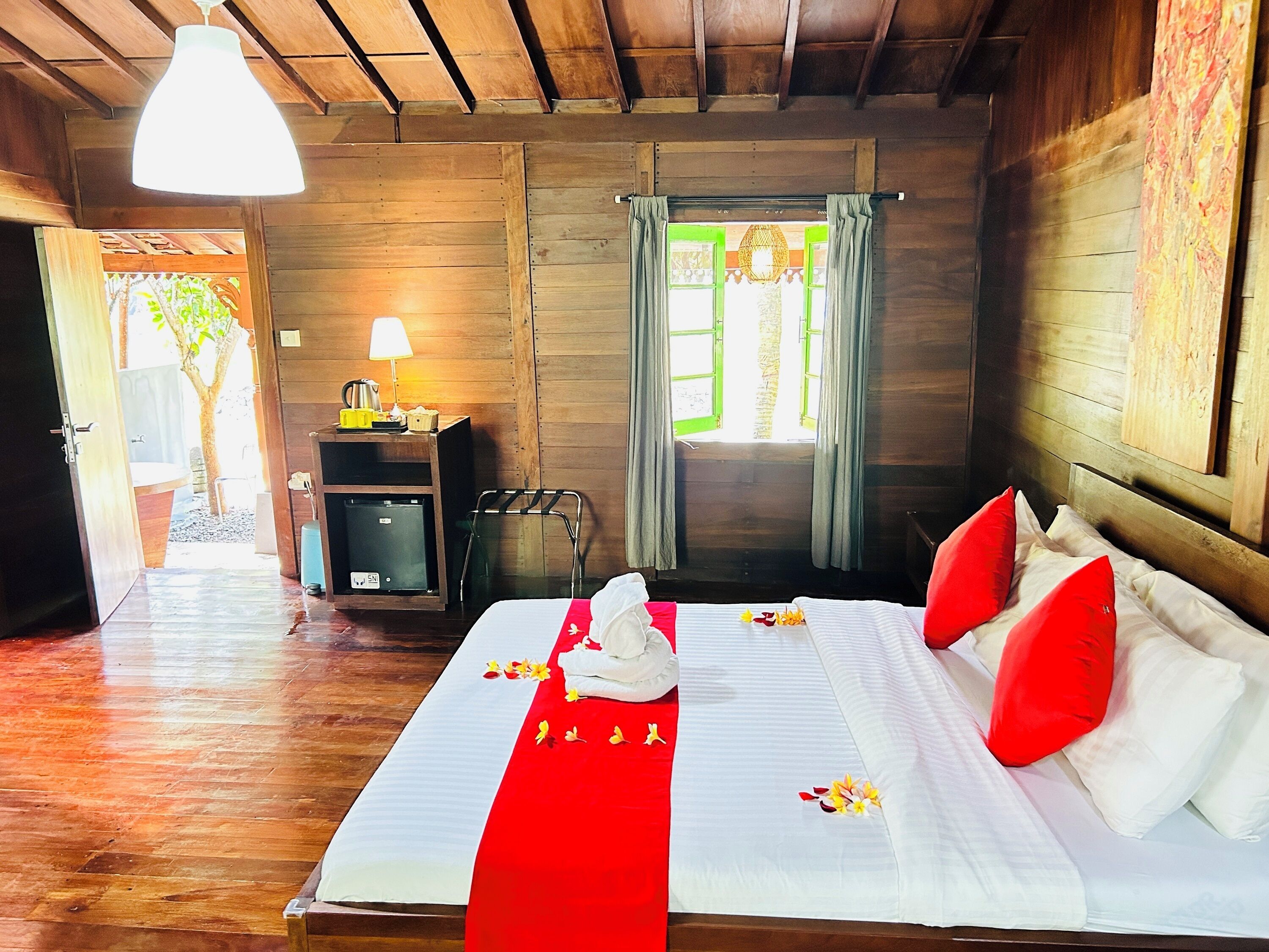 Una habitación de madera con una cama, una mesita con una lámpara y una ventana con cortinas.
