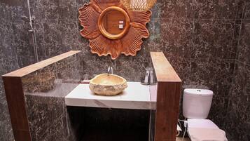 Un baño con lavamanos de mármol, lavamanos de madera, ducha y retrete.
