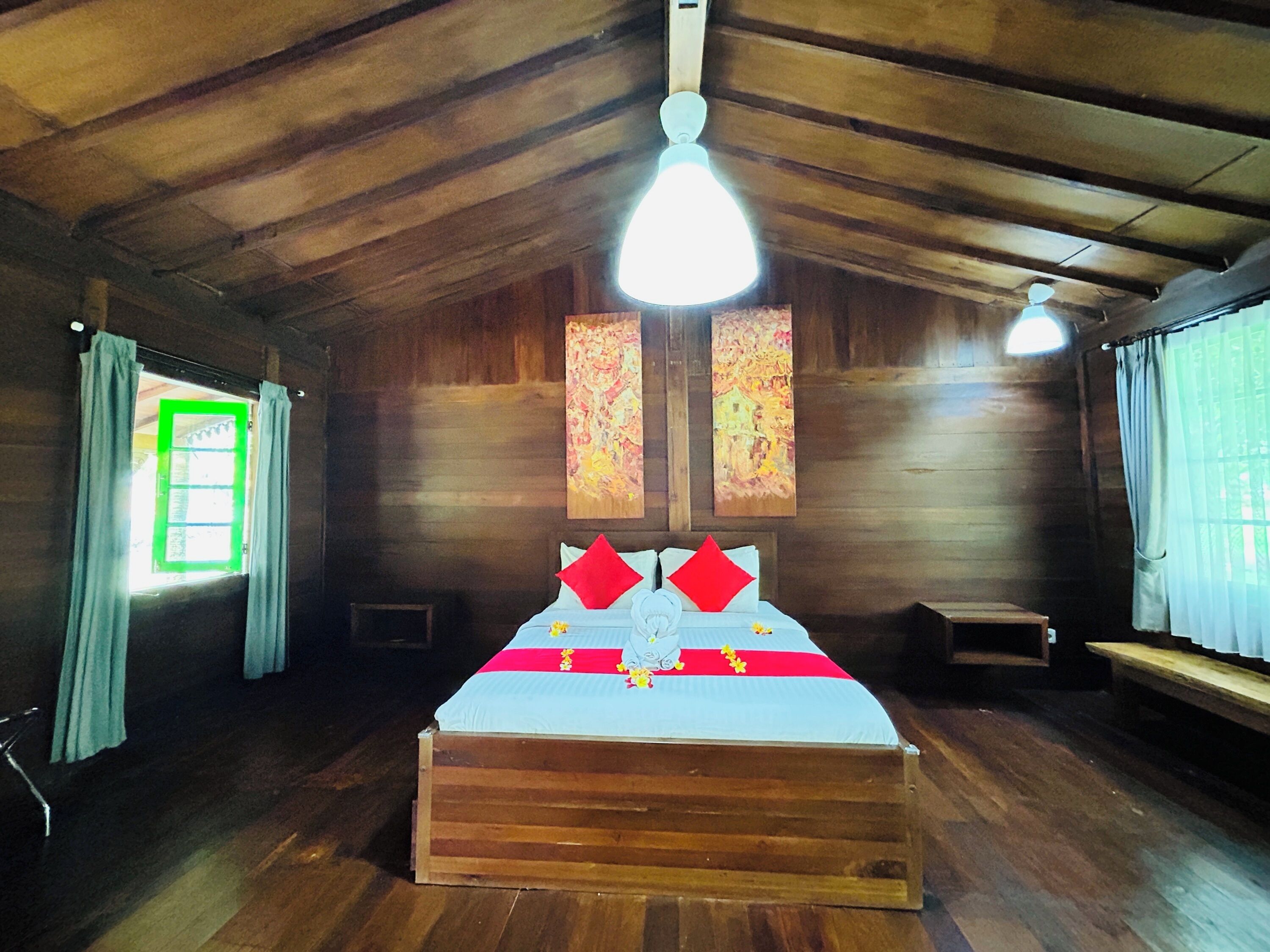 A wooden room with a bed, a window with curtains, and a ceiling fan.