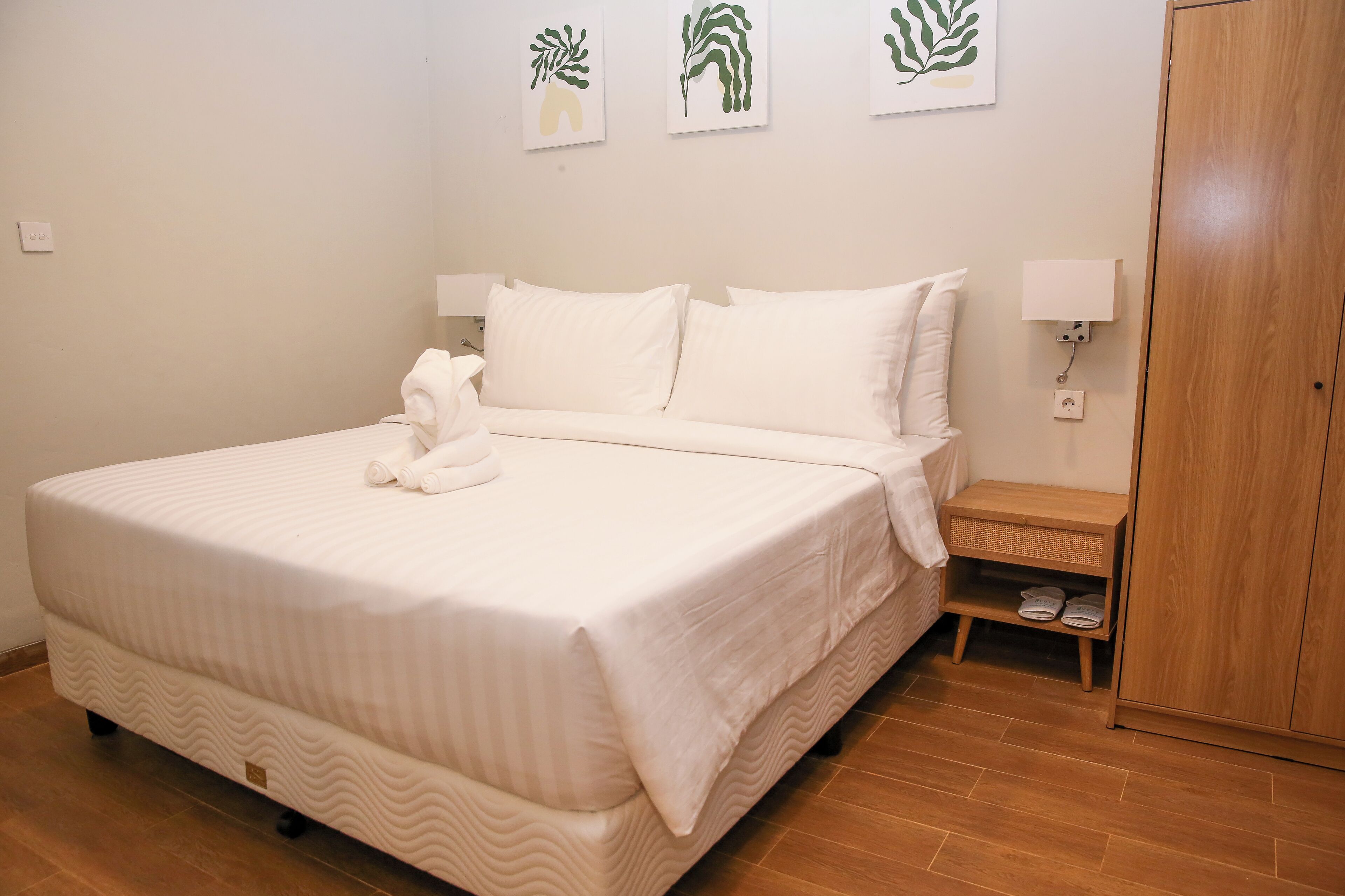 A neatly made bed with white linens, a bedside table with a lamp, and a wooden wardrobe.
