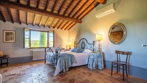 Ein Schlafzimmer mit einem großen Bett, einer Holzbalkendecke, einem Fenster mit Aussicht, einem Heizkörper, einem Spiegel und einem Stuhl.