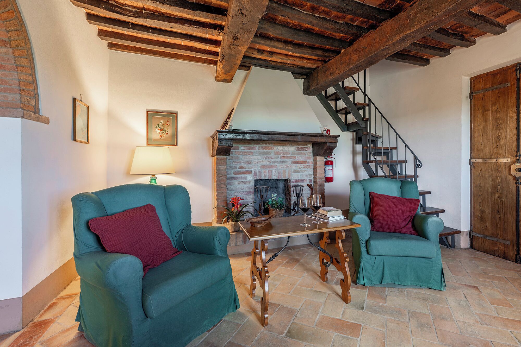 A cozy living room with two teal armchairs, a wooden coffee table, a fireplace, and a wooden staircase.